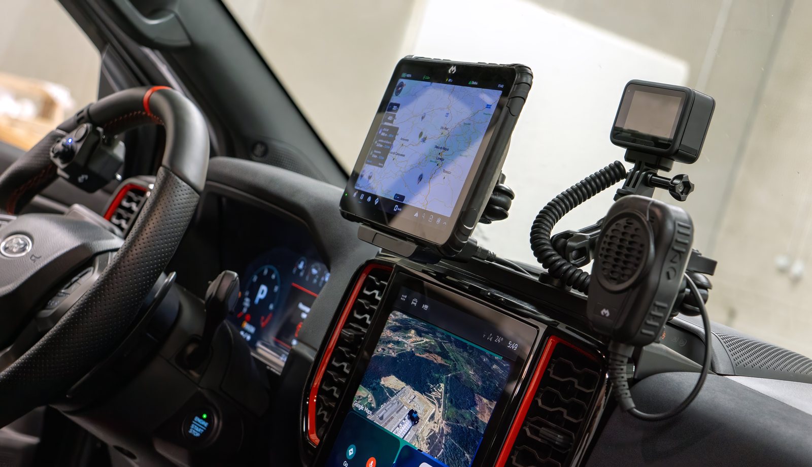 A DMD tablet mounted on a 4x4 dashboard next to the radio handset and an action camera, showing the map